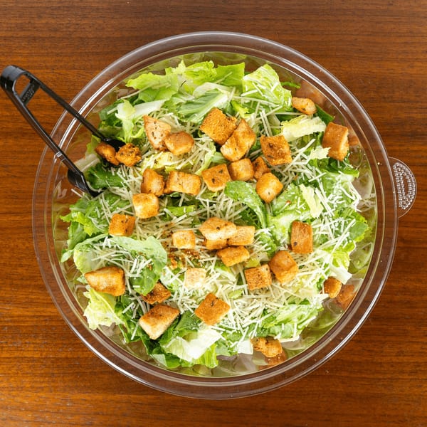 Caesar salad with fresh romaine, shredded Parmesan, and croutons in a clear bowl with tongs.