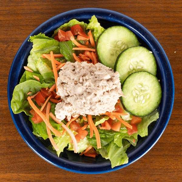 A blue bowl of Paradise Bakery and Cafe's tuna salad with lettuce, carrots, tomatoes, and cucumbers.