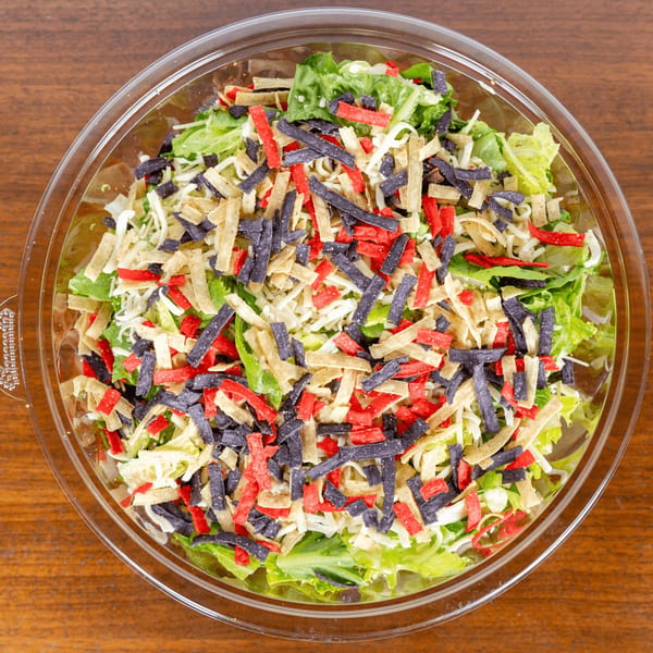 A vibrant salad in a clear plastic container, topped with red, blue, and tan tortilla strips.