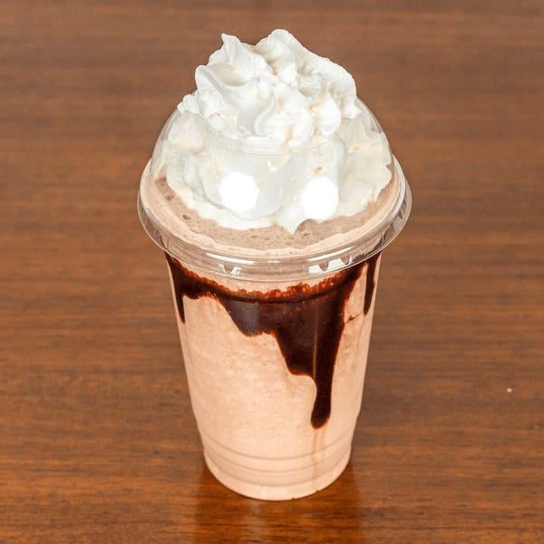 A chocolate milkshake with whipped cream and chocolate syrup drizzle in a clear plastic cup.