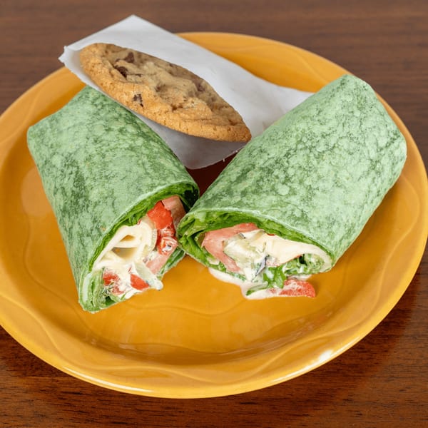 Two halves of a green spinach wrap with vegetables and sauce, and a chocolate chip cookie.