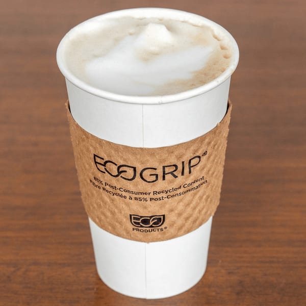 A white Paradise Bakery and Cafe coffee cup with a brown EcoGrip sleeve, filled with frothy latte.