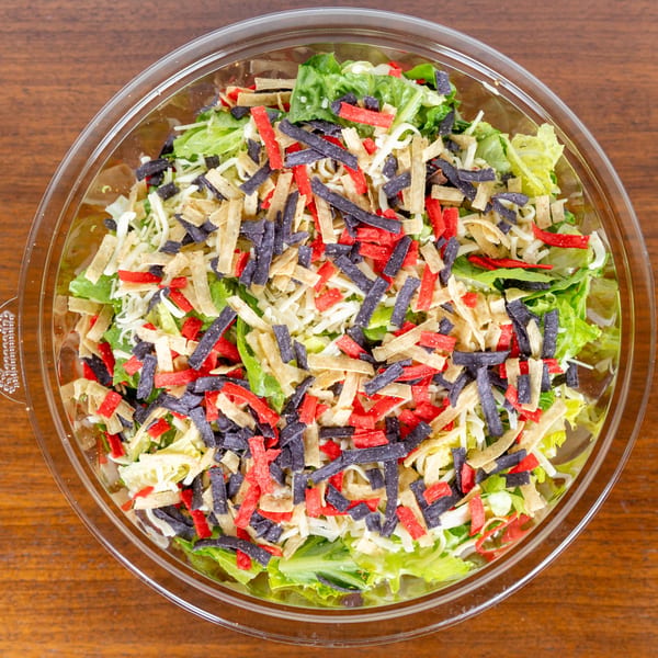 A vibrant salad with green lettuce, shredded cheese, and colorful tortilla strips in a clear bowl.