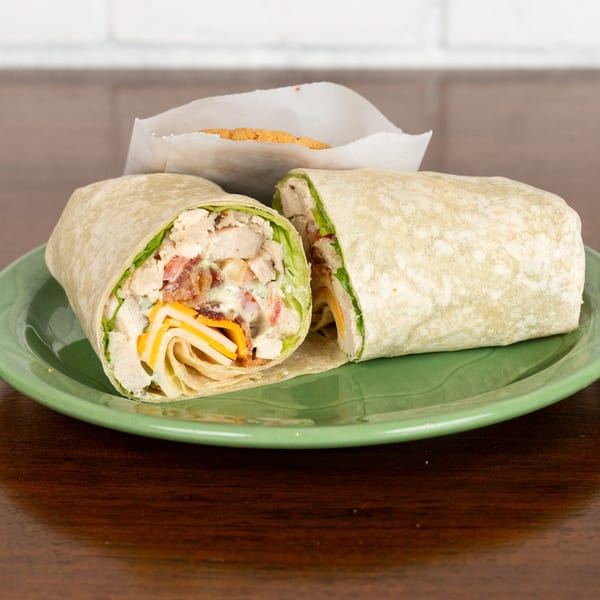 A chicken bacon ranch wrap, cut in half, on a green plate with a cookie in the background.