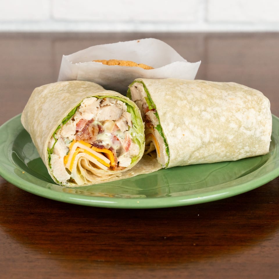 A chicken bacon ranch wrap, cut in half, on a green plate with a cookie in the background.